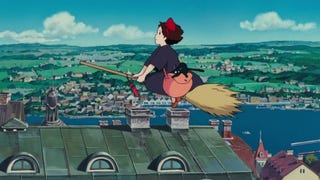 Kiki, a young girl wearing a simple dress and a red bow on her head, is flying on a broomstick with her black cat sat with her over a picturesque town.